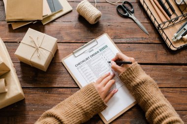 Ahşap masa üzerinde kadın ellerinin kalem tutarak genel görünümü kontrol listesine işaretlenmiş nesnelerin karşıtlığını koyarak