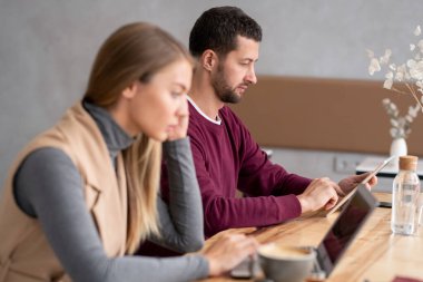 Kafe 'de ahşap masada otururken elektronik dokümanları ya da çevrimiçi verileri karıştıran dokunmatik defteri olan ciddi bir genç adam.