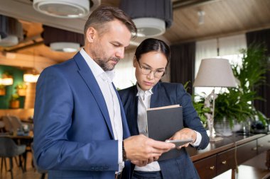 Formalite içinde iki ciddi meslektaş dokunmatik bilgisayarda elektronik belge okurken, biri ekranda kayıyor.