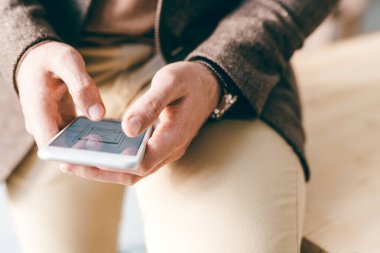 Genç ve çağdaş iş adamı akıllı telefondaki elektronik belgeleri karıştırırken masanın kenarında oturuyor.