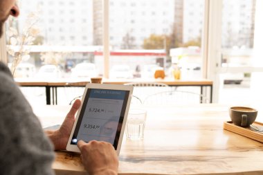 Genç adam kafede masada otururken dokunmatik ped kullanıyor ve online bankacılık bilgilerini karıştırıyor.