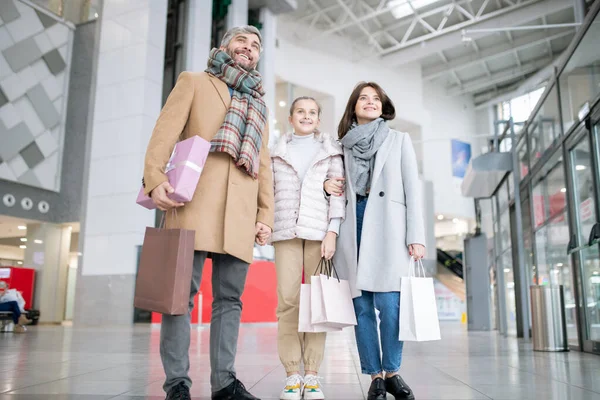 大規模な貿易センターで一緒に時間を過ごしながら 紙袋を運ぶコートで3人の若い陽気な家族 — ストック写真
