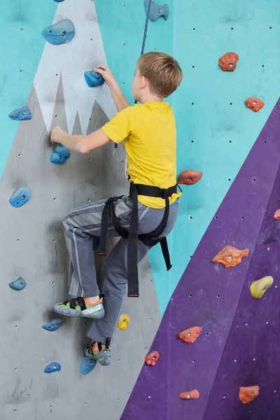 屋内トレーニング中に小さな岩につかまっている間活動的な登山の壁に若い男の子の側面図 — ストック写真