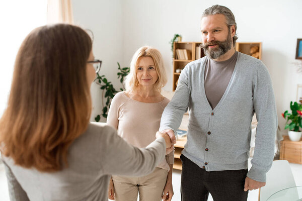 Mature casual couple greeting their real estate advisor in office while going to look for new flat or house