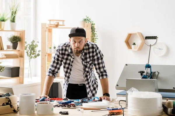 Jovem Artesão Casual Olhando Para Você Enquanto Dobra Sobre Mesa — Fotografia de Stock