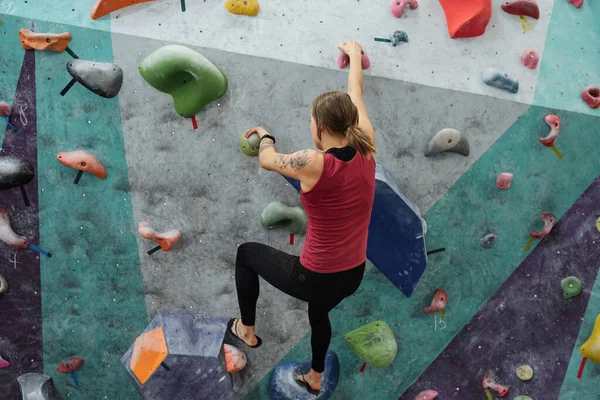 上に移動しながら壁に登る上に小さな岩につかまってアクティブな姿の若いスポーツウーマンの背面図 — ストック写真