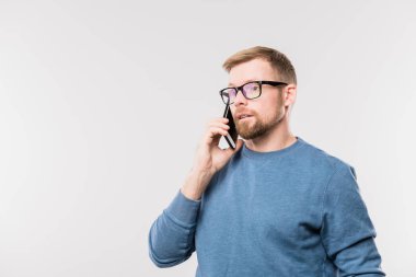 Mavi kazaklı, sakallı genç bir ajan kameranın önünde müşterilerden biriyle konuşurken kulağından akıllı telefon tutuyor.