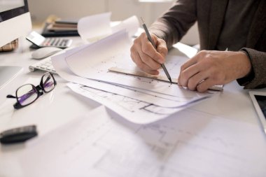 Hands of architect with pencil and ruler drawing line while working over sketch of new building project by workplace clipart