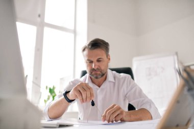 Ofiste yeni çizimler üzerinde çalışırken beyaz gömlekli, olgun sakallı bir mühendis bölücü kullanıyor.