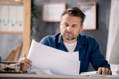 Ofiste çalışırken günlük giyimde ciddi bir mimar çizimleri kontrol ediyor.