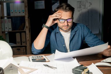 Akşam geç saatlerde masada otururken gözlüklü ciddi bir mühendis taslağı kontrol ediyor.