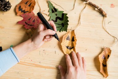Cadılar bayramına hazırlanırken kuru yaprakların üzerine siyah fosforlu yüzler çizen kadınların elleri