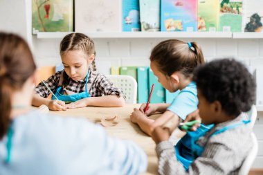 Bir grup çalışkan öğrenci masa başında oturup kağıtları çizerken bayram için cadılar bayramı süslemeleri yapıyorlar.