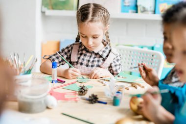 Genç yaratıcı kız sınıf arkadaşlarının yanında oturuyor ve tatilden önce el yapımı Noel süsleri çiziyor.