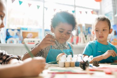 Ciddi bir okul çocuğu ve sınıf arkadaşı ders sırasında masa başında oturup Noel süslerini balıkla boyuyor.