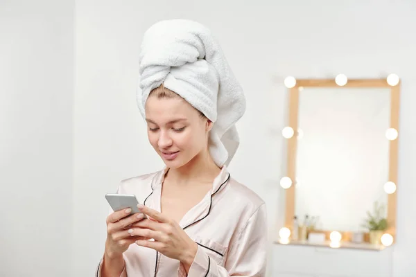 頭の上に柔らかい白いタオルで若いきれいな女性は 朝のシャワーの後 スマートフォンでメッセージをスクロール — ストック写真