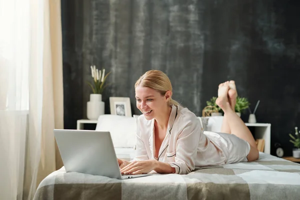 Fiatal Szőke Mosolygós Selyem Pizsamában Aki Laptopot Néz Maga Előtt — Stock Fotó