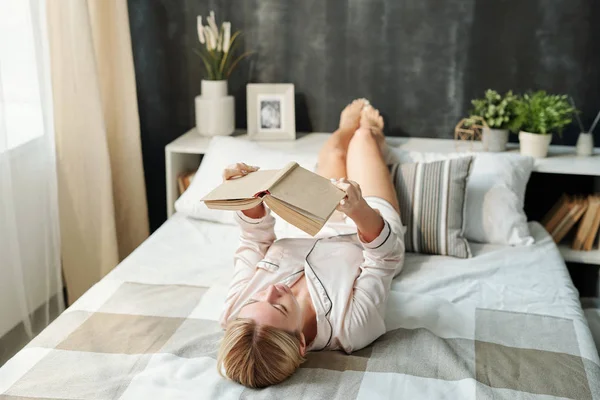 Ξανθό Κορίτσι Πιτζάμες Ξαπλωμένη Στο Κρεβάτι Και Διαβάζοντας Βιβλίο Ενώ — Φωτογραφία Αρχείου