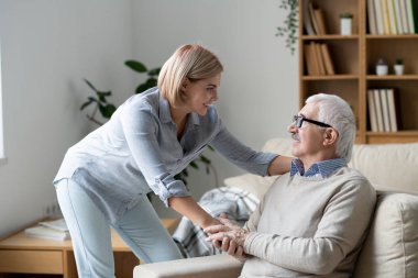 Mature casual man on couch holding hand of his daughter while looking at her during chat in home environment