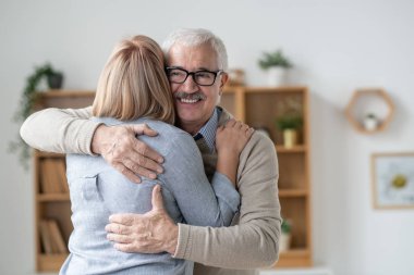 Happy and affectionate senior man giving hug to his blonde young daughter while expressing love
