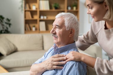 Sick retired man with grey hair holding hand of his young careful daughter bending to him while standing near by