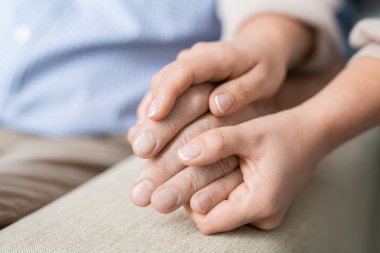 Hands of young affectionate and careful daughter holding that of her senior father expressing love and togetherness