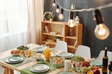Thanksgiving or Christmas festive dinner on table with lamps hanging above on background of shelves
