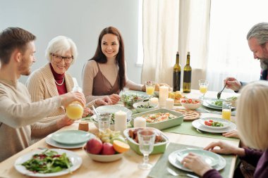Young man pouring orange juice for his granny during family dinner by served festive table on Thanksgiving day