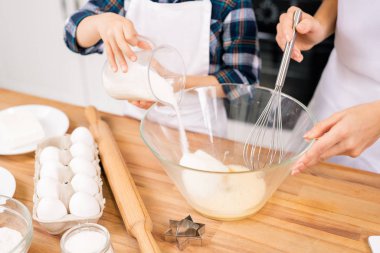 Mutfakta ev yapımı hamur işleri için annesine yardım ederken çiğ yumurtalarla kaseye küçük çocuk şekeri koyuyor.