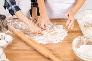 Hands of mother and son drawing on wooden table with flour while going to knead dough and make cookies or other pastry