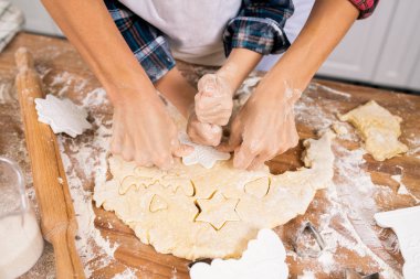 Hands of mother and son cutting cookies from rolled dough while cooking pastry for Christmas dinner