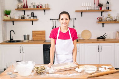 Happy young female standing by table in the kitchen while going to make cookies with lemon for her family