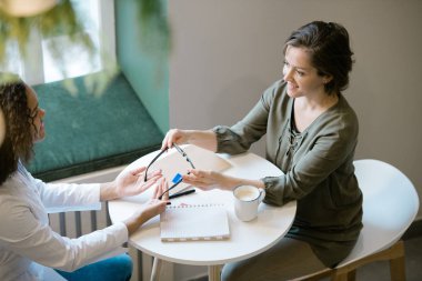 Attractive woman looking at optics clinician while going to buy pair of new eyeglasses and listening to recommendations