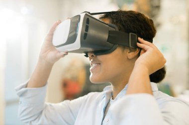 Young mixed-race woman taking on vr headset on head to watch presentation of new assortment and choose product