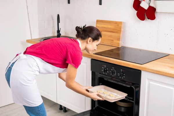 Fiatal Háziasszony Kötényben Teszi Tálca Nyers Cookie Kat Nyitott Sütőbe — Stock Fotó