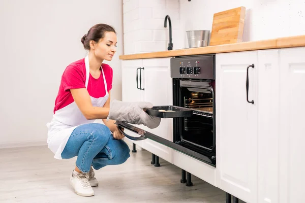 Young Housewife Apron Squatting While Putting Tray Raw Cookies Electric — 스톡 사진