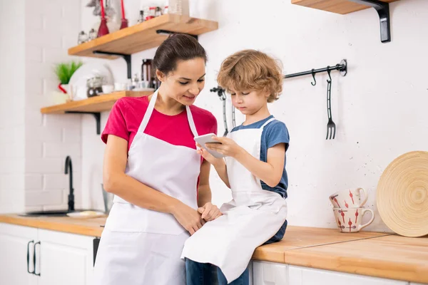 Curly Blond Boy Apron Showing His Mother Recipe Smartphone While — Stockfoto
