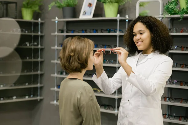 Junger Lächelnder Berater Des Optikgeschäfts Hilft Dem Kunden Beim Anprobieren — Stockfoto