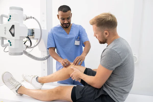 Contemporary Clinician Uniform Massaging Sick Knee Young Man Hospital Examining — Stok fotoğraf