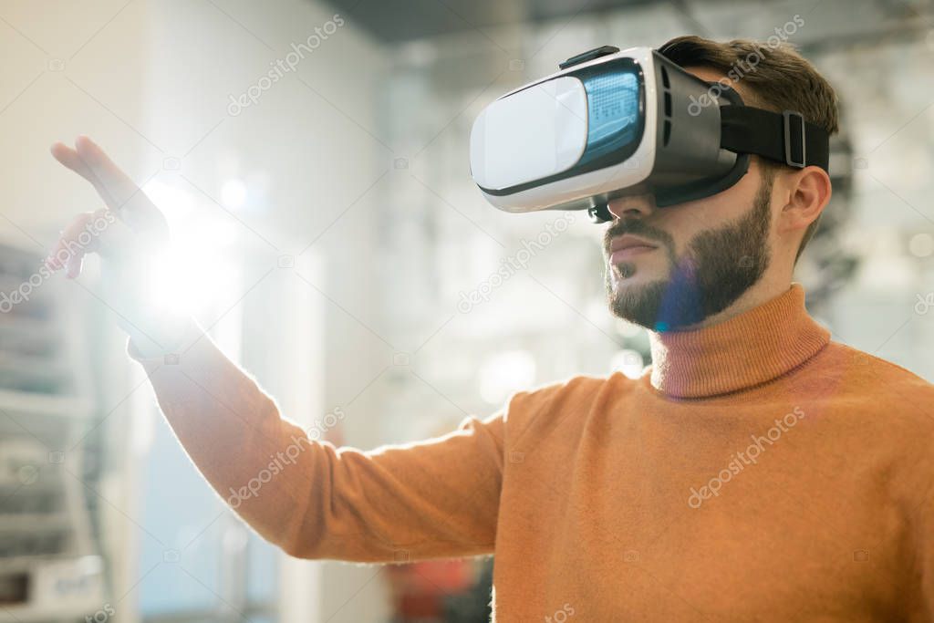 Serious young man in vr goggle touching virtual display while making presentation or looking through new collection