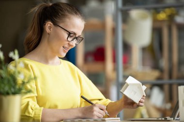 Başarılı genç bayan mimar elinde ev modeliyle yeni proje üzerinde çalışırken notlarına bakıyor.