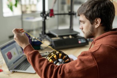Genç ciddi tasarımcı yeni nesnenin 3 boyutlu baskısını yaparken sarı ipliği makaradan geriyor.