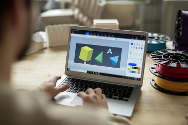 Dizüstü bilgisayarda çeşitli geometrik şekiller ve ofiste çalışırken klavye üzerinde yaratıcı tasarımcının elleri