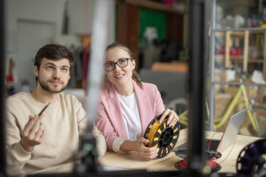 İki genç yaratıcı tasarımcı 3D yazıcıya bakarken iş yerinde onun özelliklerini ve modelini tartışıyor.