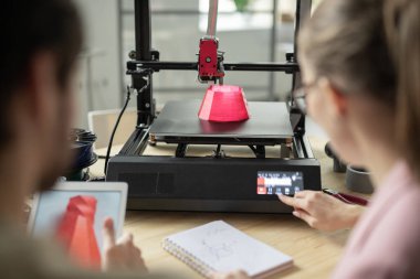 Genç yöneticilerden biri pembe nesne yazdırma işlemi sırasında 3D yazıcının kontrol panelinde düğmeye basıyor
