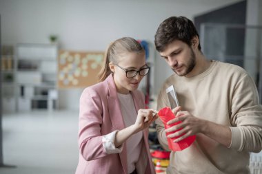 İş kadını bir şey açıklarken genç meslektaşlar 3 boyutlu yazıcıda kırmızı geometrik nesneleri tartışıyor.
