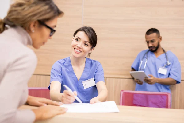 Hübsche Ärztin Uniform Lächelt Patientin Während Sie Auf Ärztliches Dokument — Stockfoto