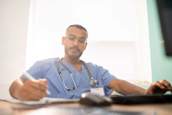 Bearded Serious Doctor Intern Uniform Making Working Notes While Sitting — Stok fotoğraf