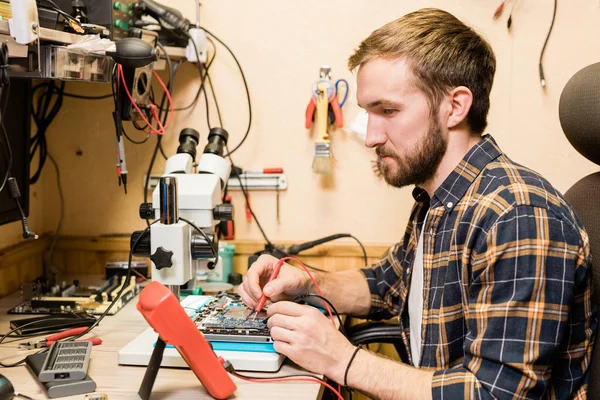 Junger Bärtiger Mechaniker Mit Zwei Lötkolben Sitzt Arbeitsplatz Der Werkstatt — Stockfoto