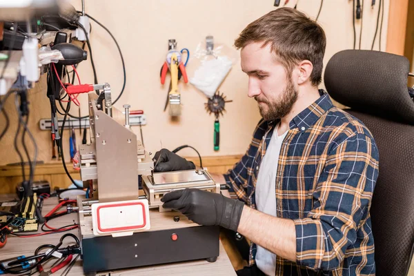 Bärtiger Reparateur Schutzhandschuhen Sitzt Arbeitsplatz Vor Geräten Für Die Reparatur — Stockfoto